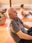 Group of people exercising. They are sat on the floor with their knees bent and their feet raised off the floor doing balance exercises
