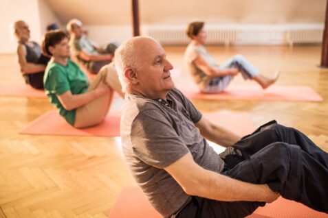 Group of people exercising. They are sat on the floor with their knees bent and their feet raised off the floor doing balance exercises