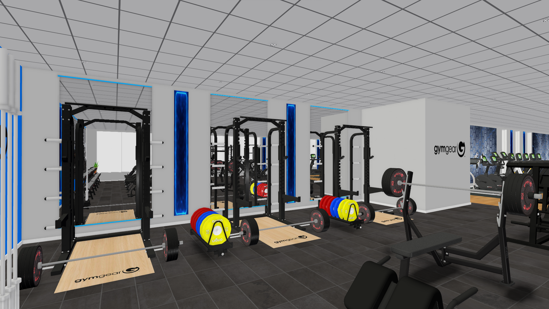 Digitally generated image to show a section of the proposed refurbished gym at Heywood Sports Village. The images shows three black squat racks with wooden lifting platforms, each equipped with Olympic barbells and colorful weight plates in red, blue, and yellow. The racks are positioned against a white wall with the GymGear logo, and the space has dark gray tiled flooring and a white grid ceiling. Blue vertical accent panels add contrast to the walls, and additional gym equipment is visible in the background.